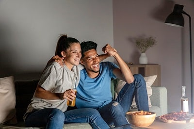 man-and-woman-having-beer-at-home-while-watching-tv-and-eating-snacks-min
