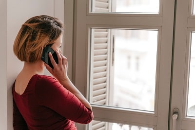 woman-speaking-on-smartphone-near-window-min